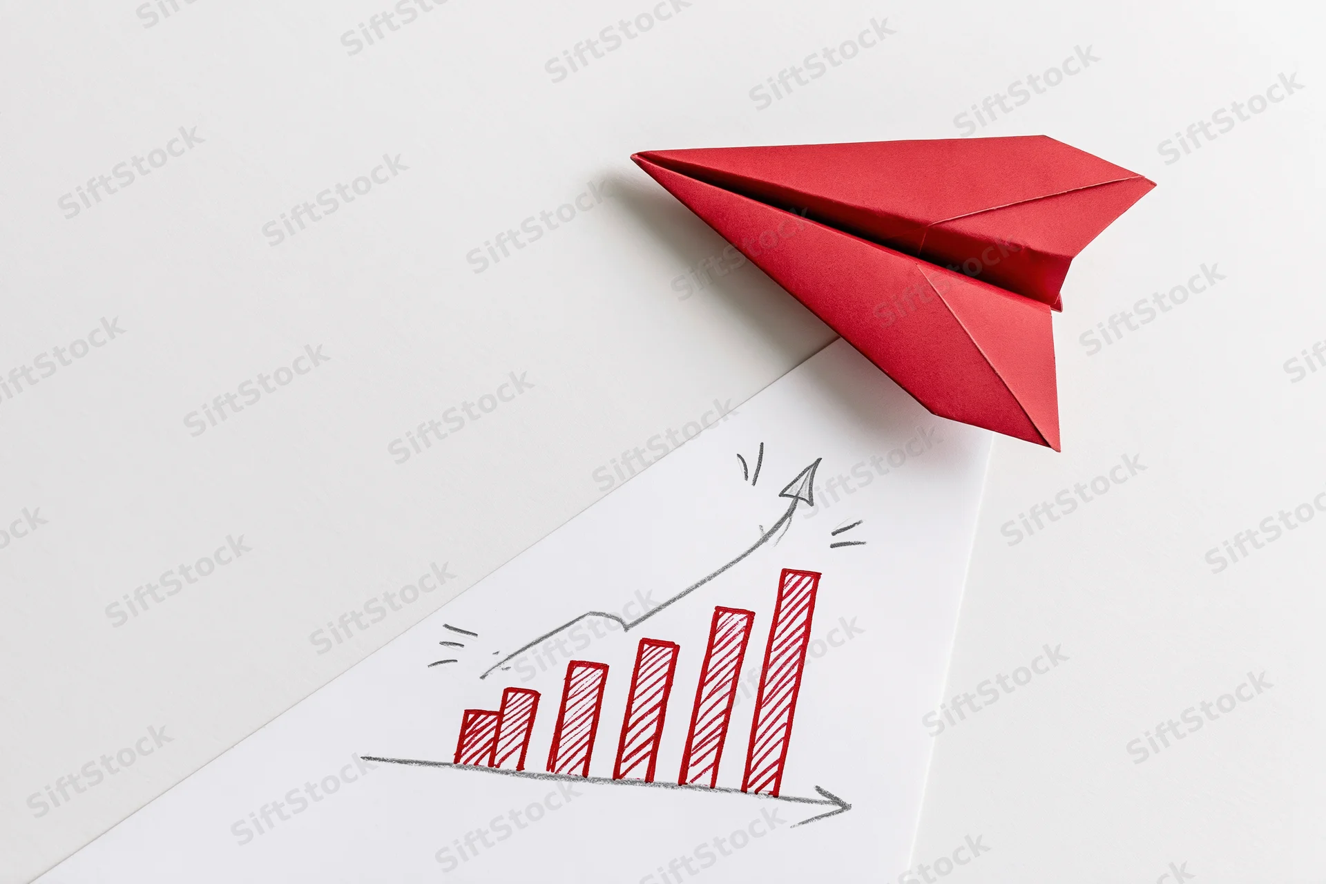 Red origami paper airplane resting on a white surface above a hand-drawn upward trending bar graph