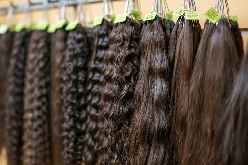 Rows of dark brown hair extensions in varying textures hanging on a rack in a salon display