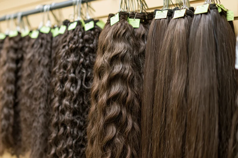 Dark brown hair extensions in curly and straight textures hanging on a display rack in a salon
