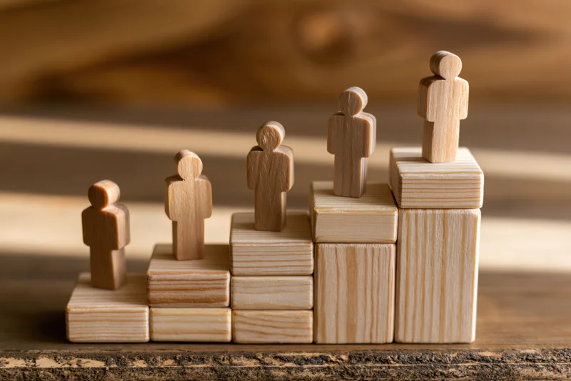 Wooden human figurines standing on ascending blocks arranged in a row on a wooden surface