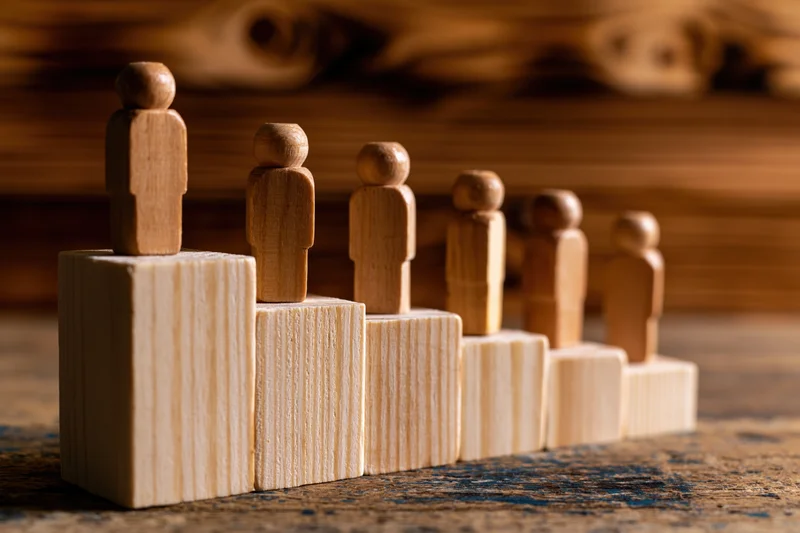 Wooden human figurines standing on ascending blocks arranged in a row on a textured surface