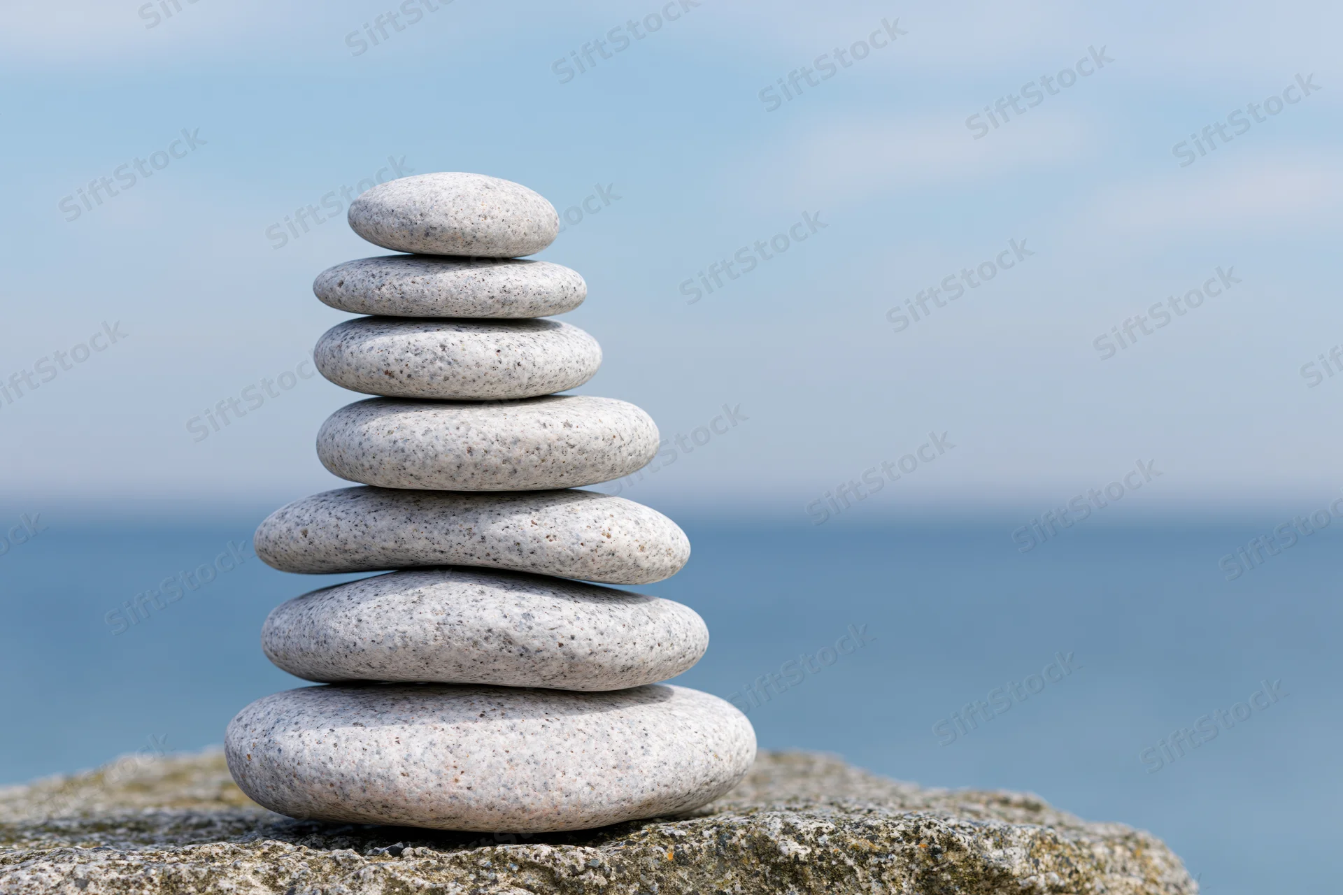 Smooth granite pebbles stacked in a balanced tower on a rocky outcrop by the ocean