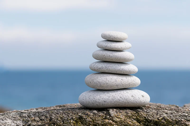 Balanced stack of smooth gray pebbles on a rocky outcrop overlooking the ocean