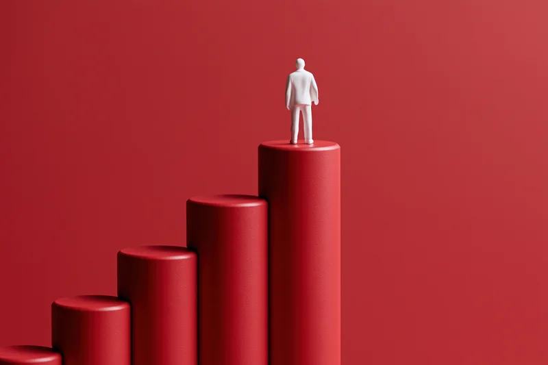 White figurine standing on top of red rising bar chart against red background
