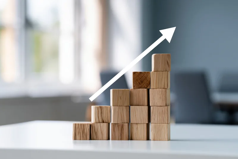 Wooden blocks stacked in ascending formation with white arrow on office desk