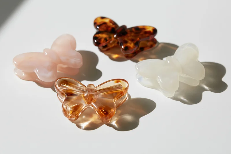 Four butterfly-shaped acetate hair claw clips arranged on a white surface with soft shadows
