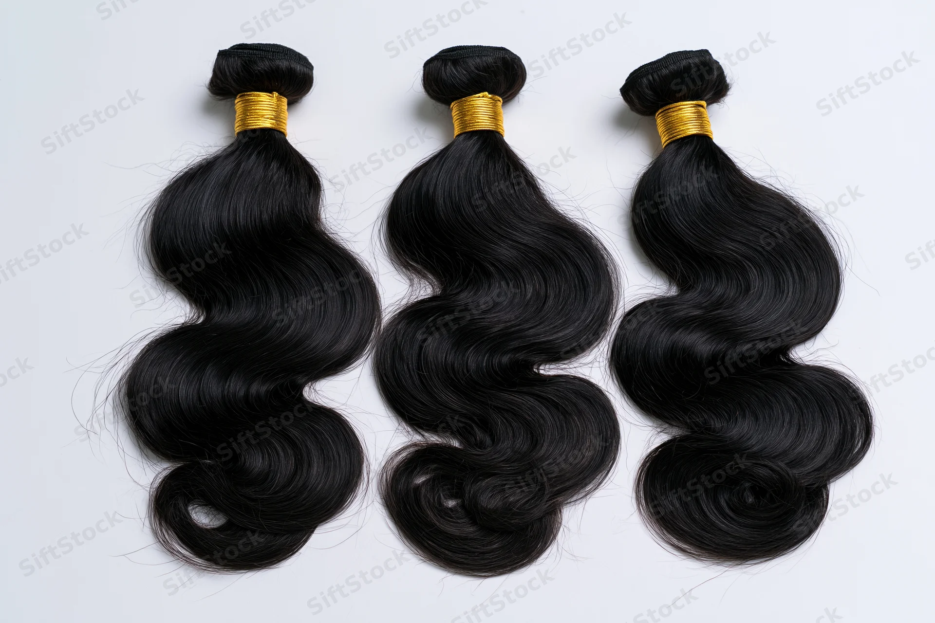 Three bundles of black body wave hair extensions laid flat on white background