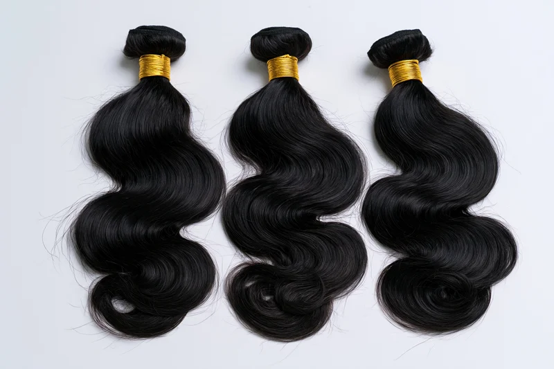 Three bundles of black body wave hair extensions laid flat on white background