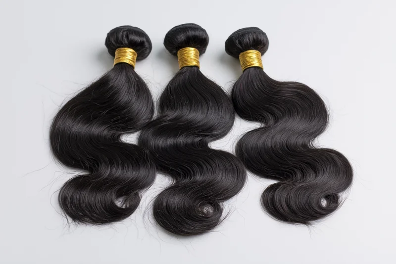 Three bundles of black body wave hair extensions laid flat on white background
