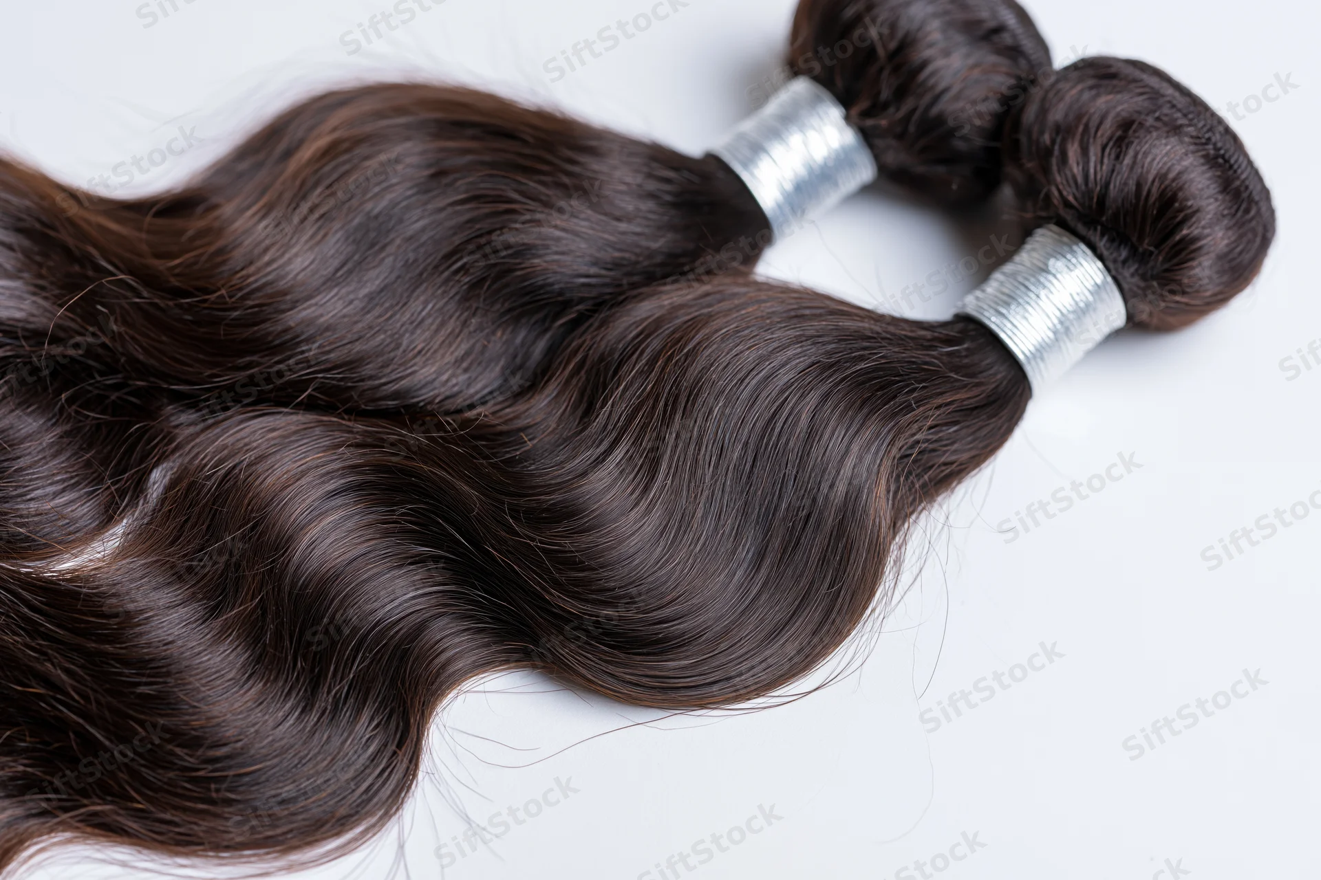 Three bundles of body wave human hair extensions with silver bands on white background