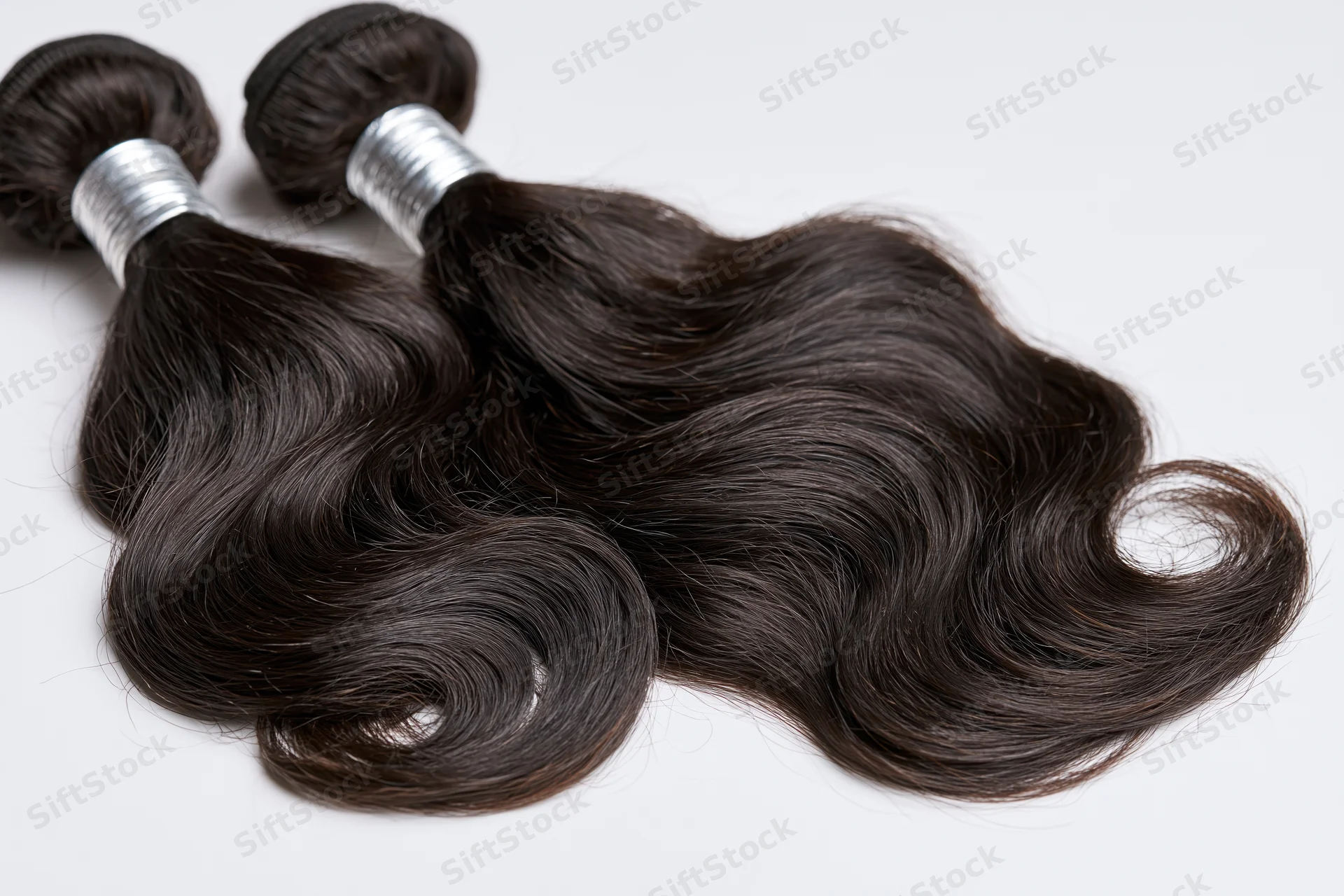Three bundles of dark brown body wave human hair extensions with silver bands on white background