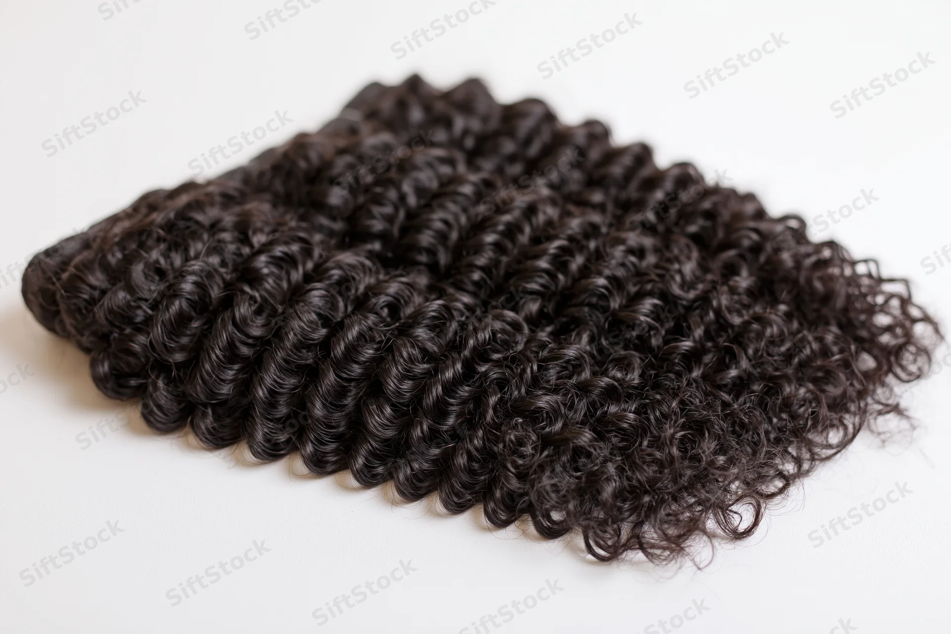 Three bundles of deep curly black hair extensions laid flat on white background