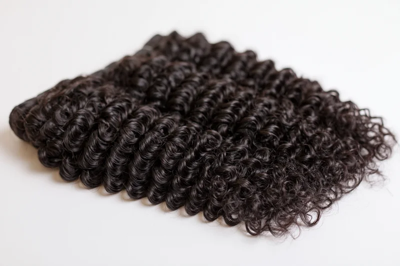 Three bundles of deep curly black hair extensions laid flat on white background