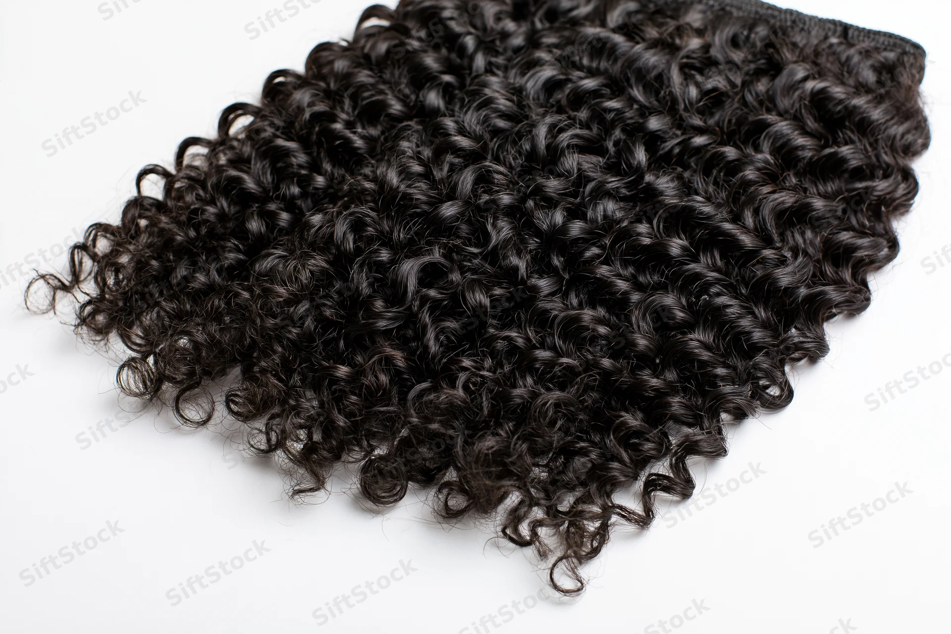 Deep curly black hair extensions laid flat on white background