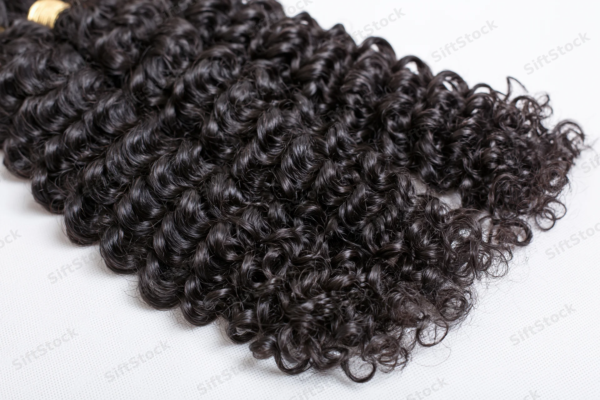 Three bundles of deep curly black hair extensions laid flat on white surface