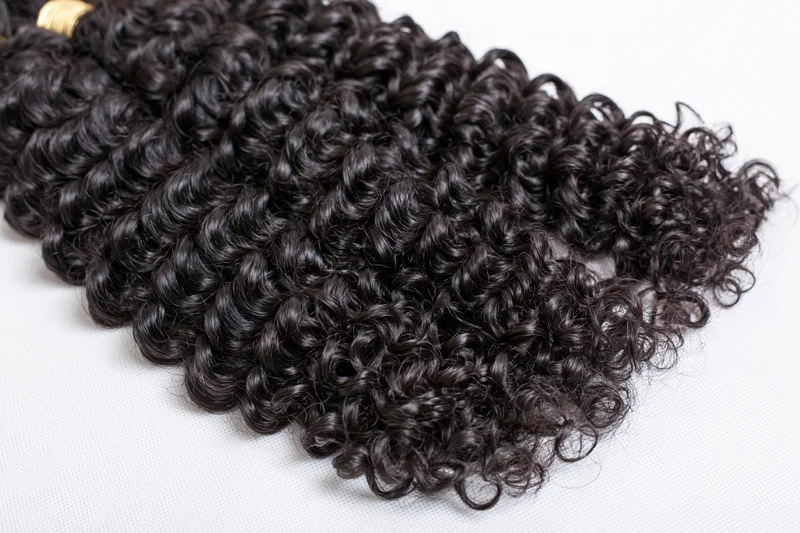 Three bundles of deep curly black hair extensions laid flat on white surface