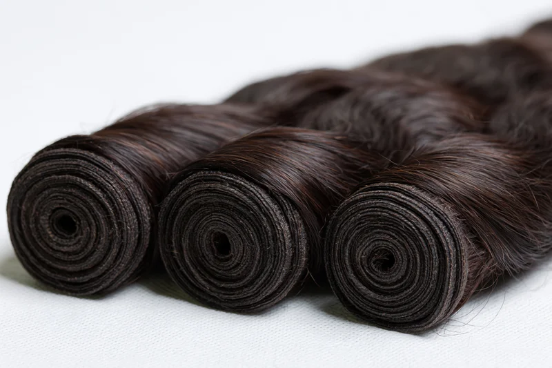 Three rolled bundles of dark body wave human hair extensions on white background