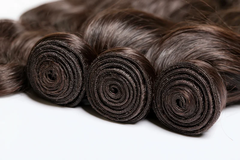 Three rolled bundles of dark body wave human hair extensions on white background