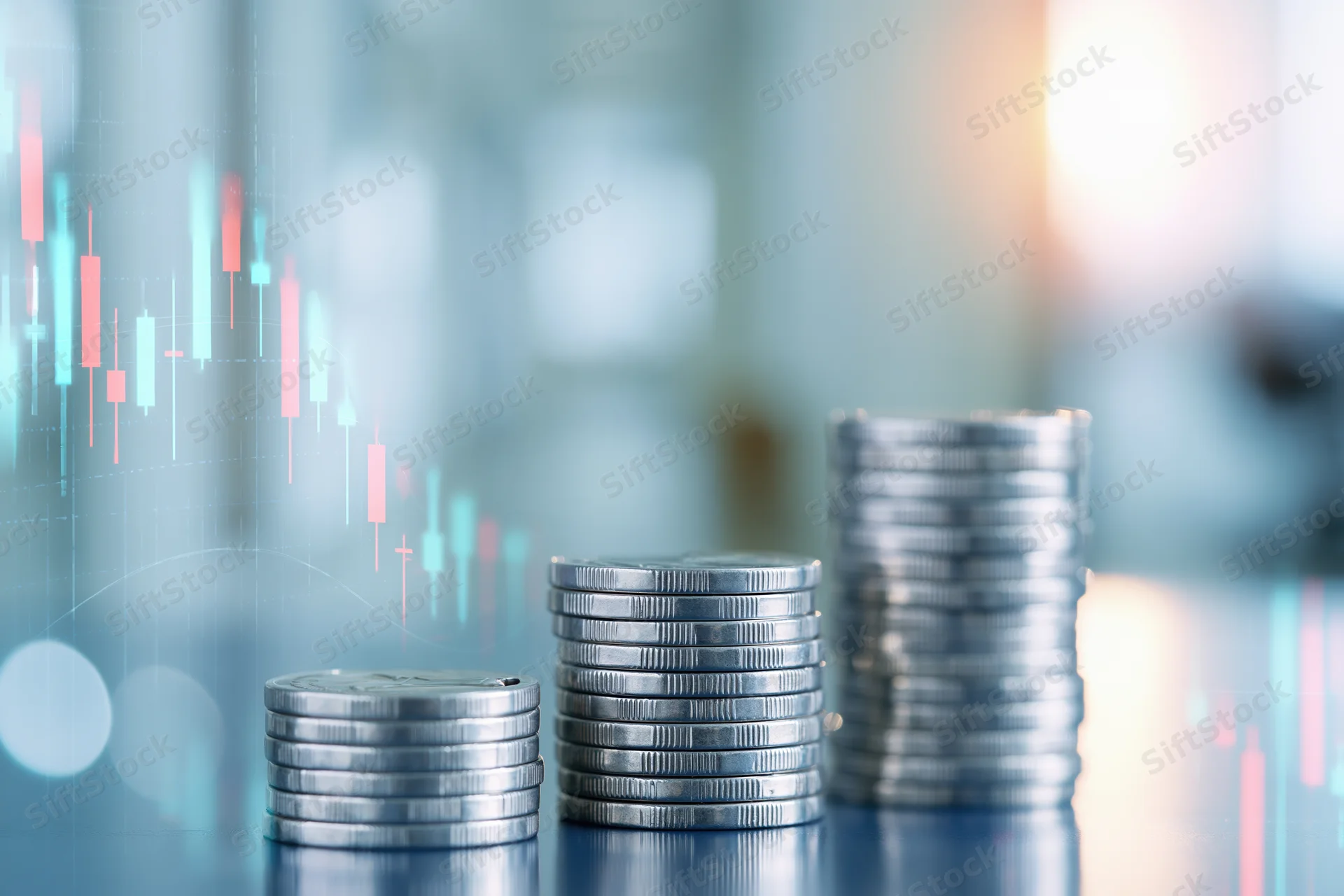 Three stacks of silver coins arranged in ascending height on a reflective surface with digital stock market charts overlaid in the background