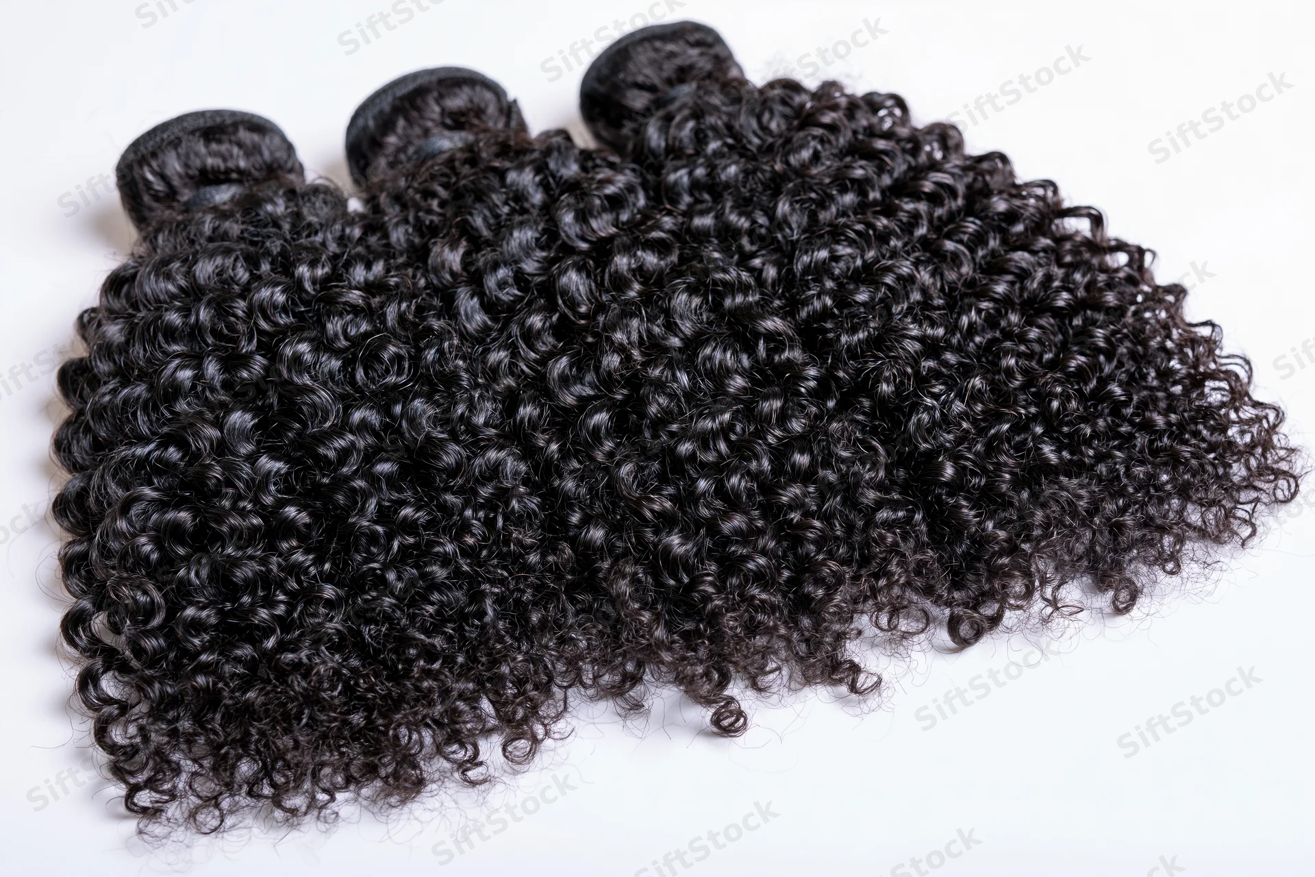 Three weft bundles of deep black kinky curly hair extensions on white background