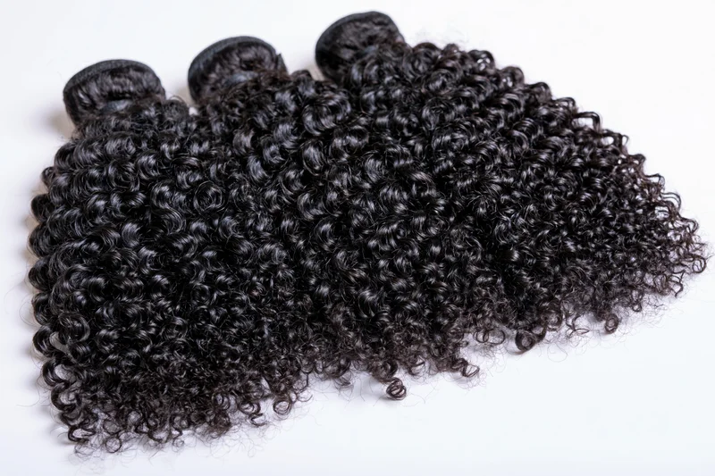 Three weft bundles of deep black kinky curly hair extensions on white background