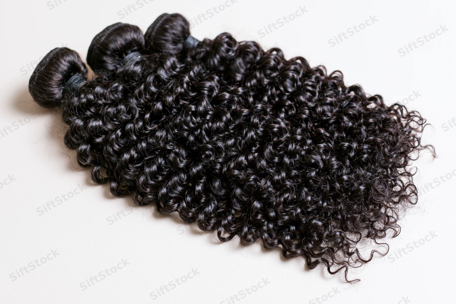Three weft bundles of deep black kinky curly hair extensions on white background
