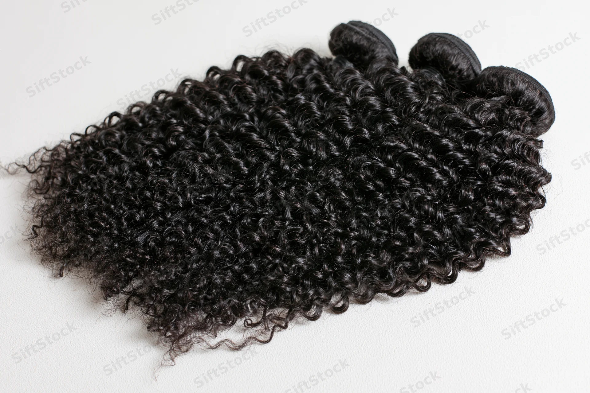 Three weft bundles of deep black kinky curly hair extensions on white background