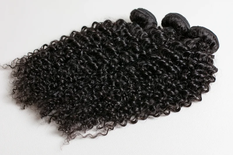 Three weft bundles of deep black kinky curly hair extensions on white background