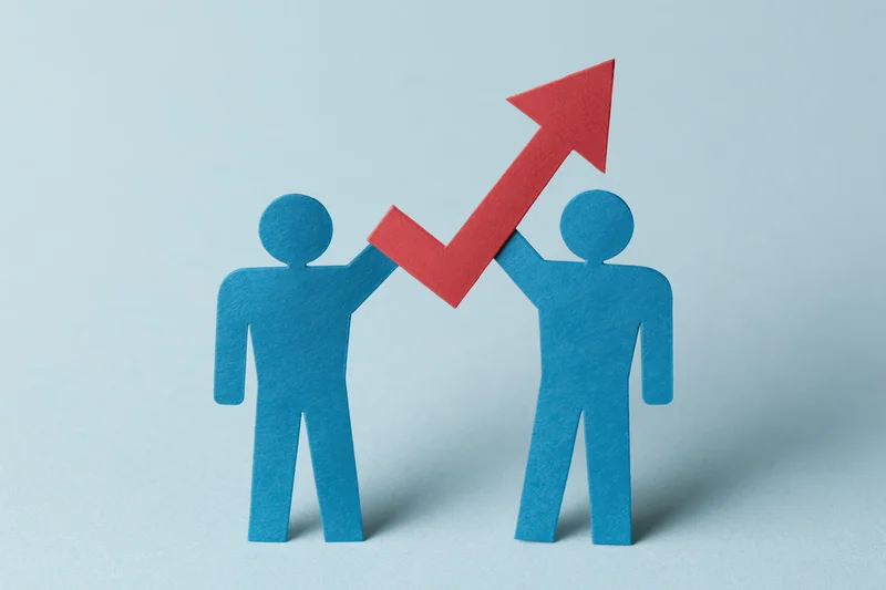 Two blue paper cutout figures holding a red upward arrow against a light blue background