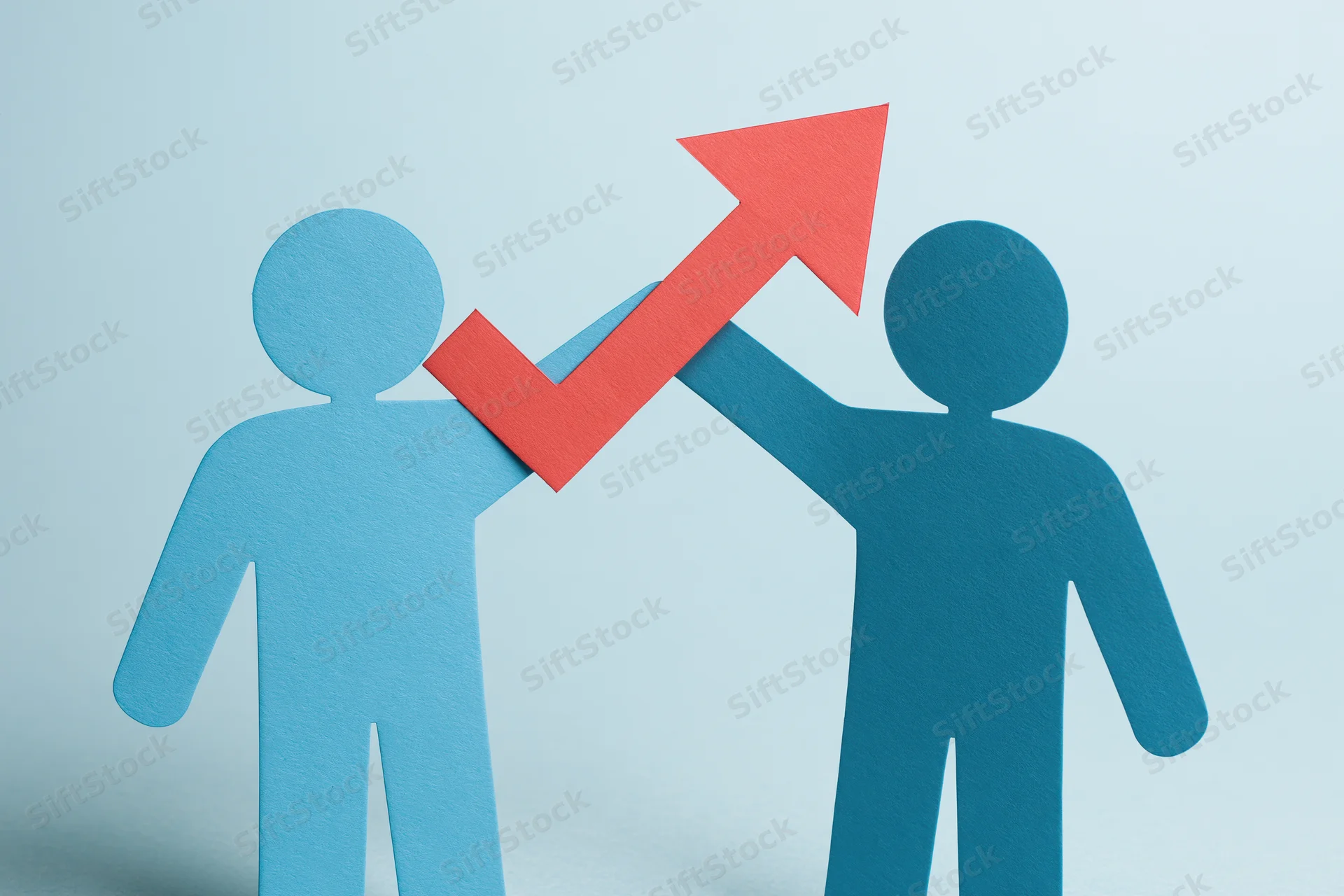 Two blue paper cutout figures holding a red upward arrow symbolizing growth and teamwork