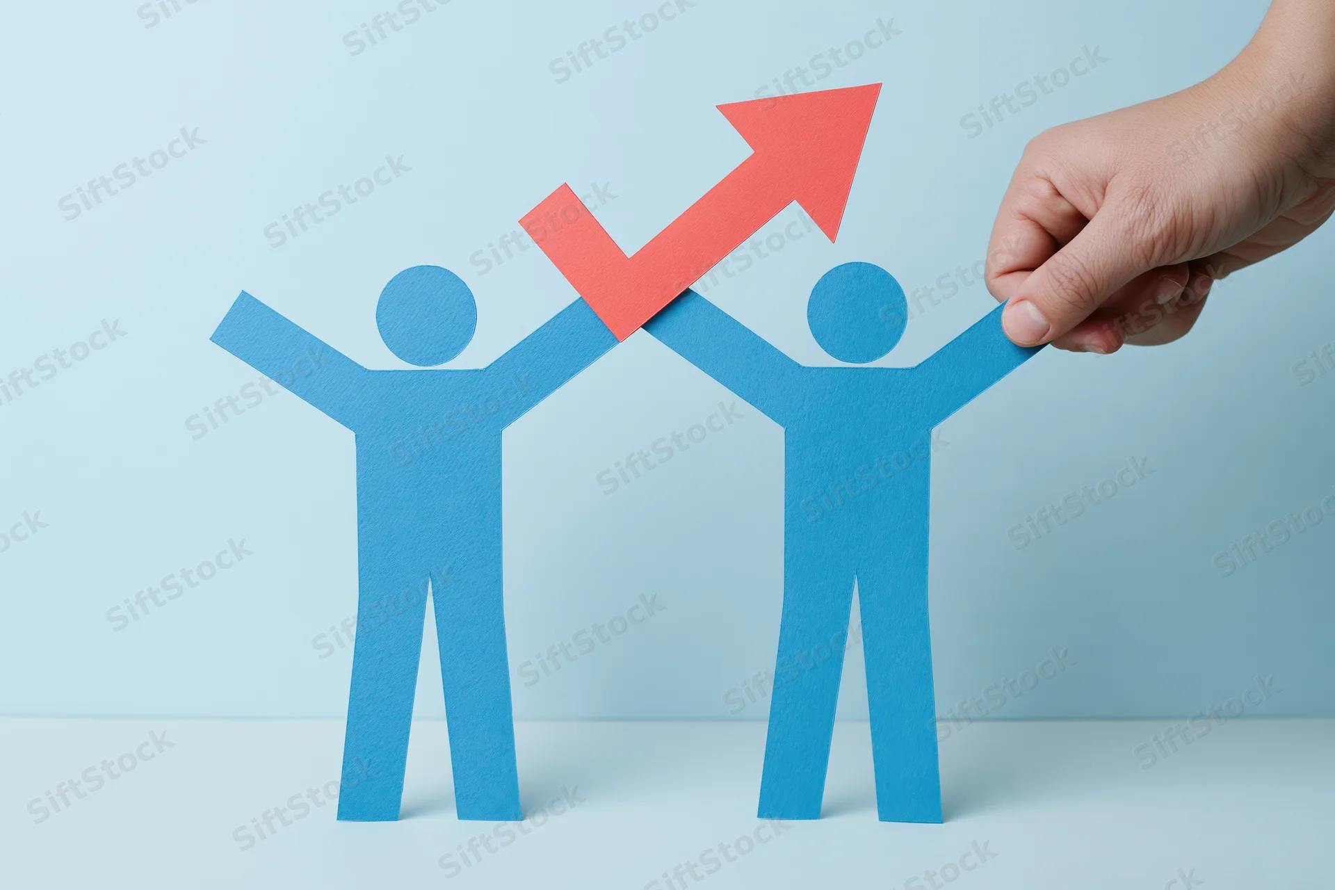 Hand lifting blue paper cutout figures holding red upward arrow on light blue surface
