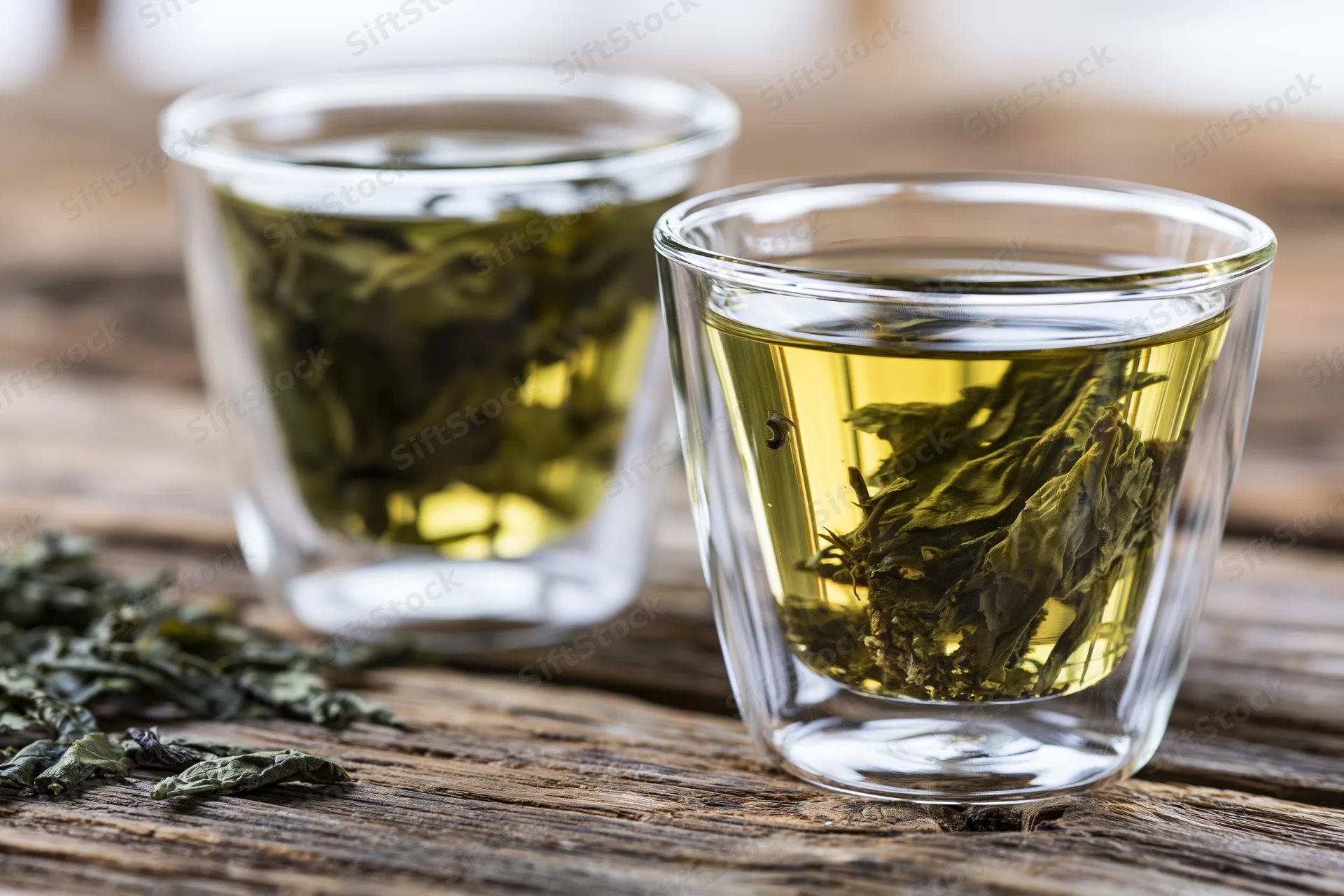 Two glass cups with steeping green tea leaves on a wooden table