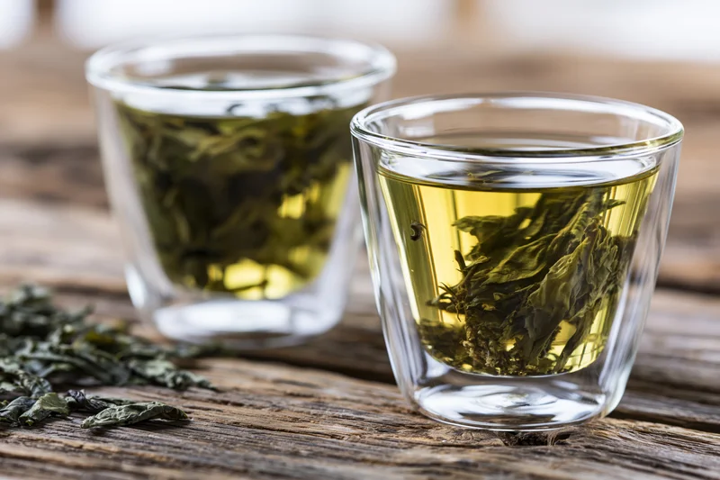 Two glass cups with steeping green tea leaves on a wooden table