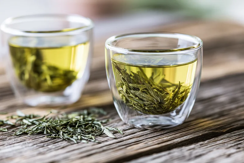 Two glass cups with steeping green tea leaves on a wooden surface