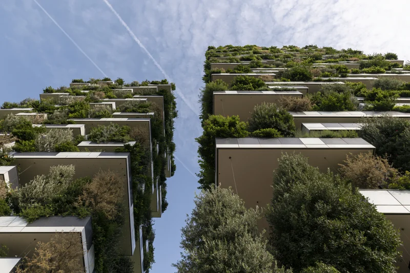 Two tall residential towers covered in greenery and trees, viewed from below against a blue sky