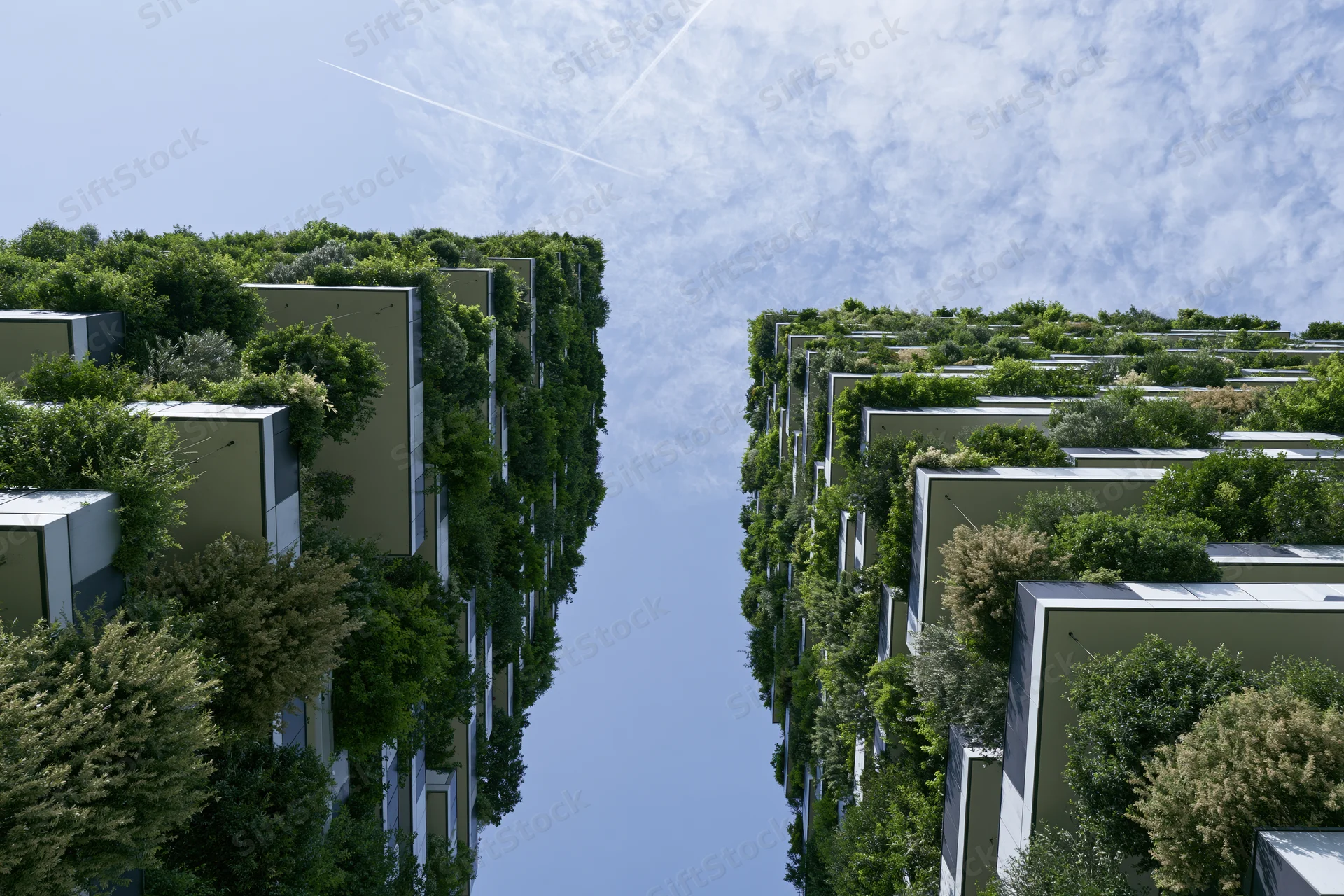 Two green-covered residential towers with dense vegetation on facades under a blue sky