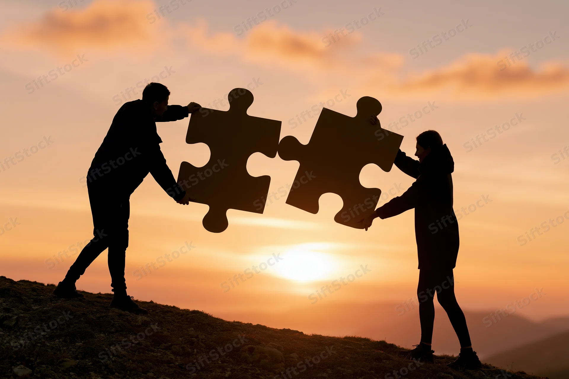 Two people connecting large puzzle pieces on a hill at sunset