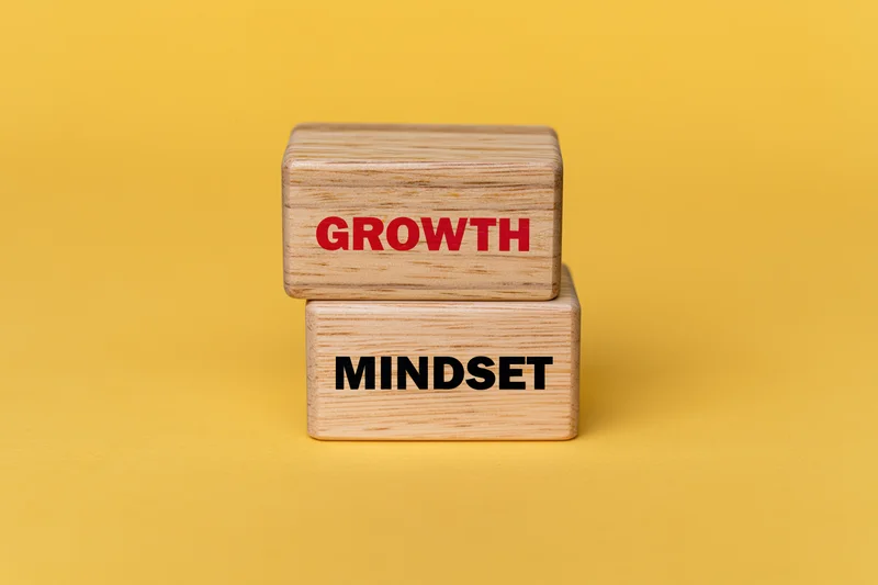 Two wooden blocks stacked offset with growth and mindset text on yellow background