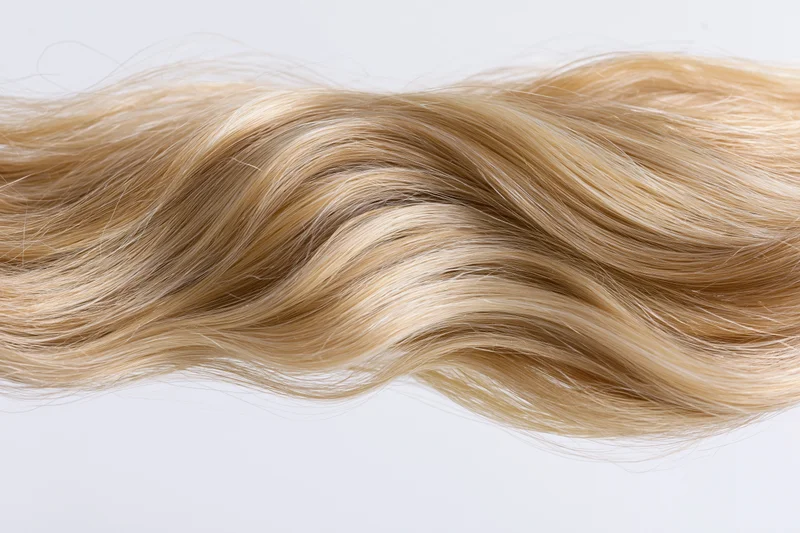Wavy blonde hair extension floating mid-air against white background