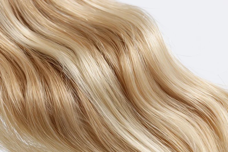 Wavy blonde hair extension floating against white background