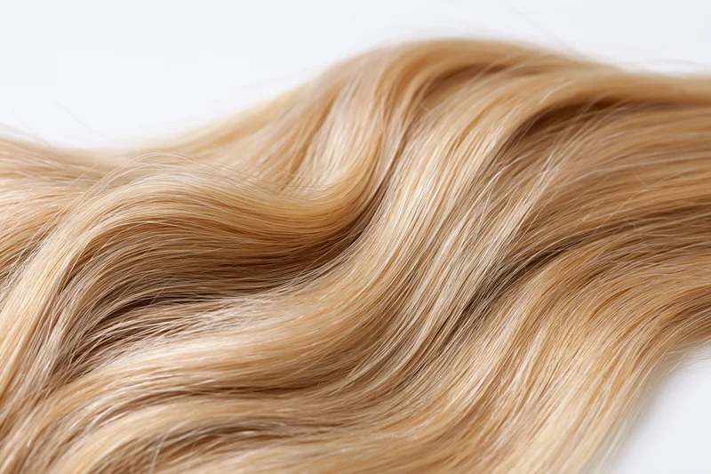 Wavy blonde hair extension floating against white background