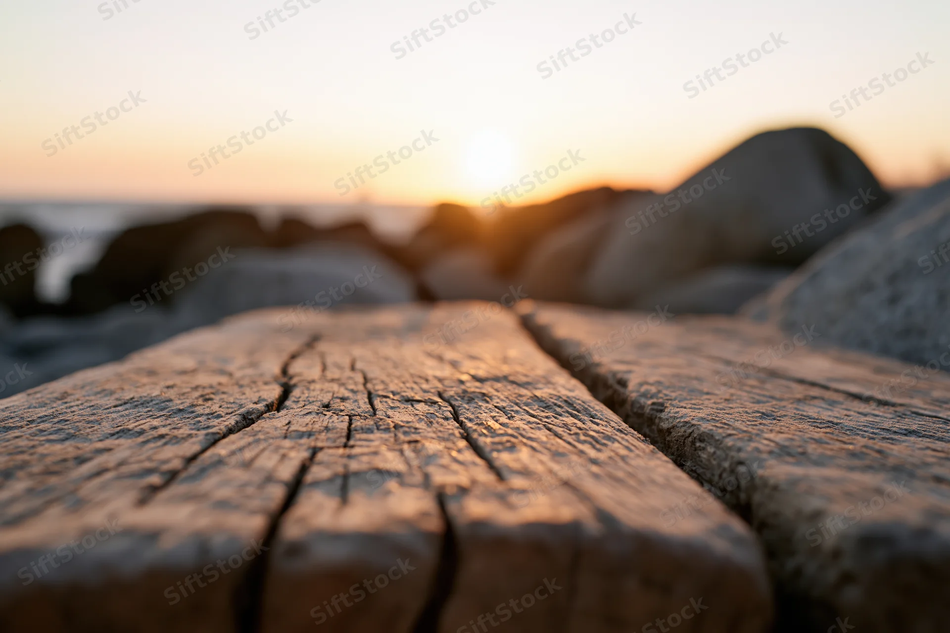 Weathered wooden planks on a beach at sunset with rocks and ocean in the background