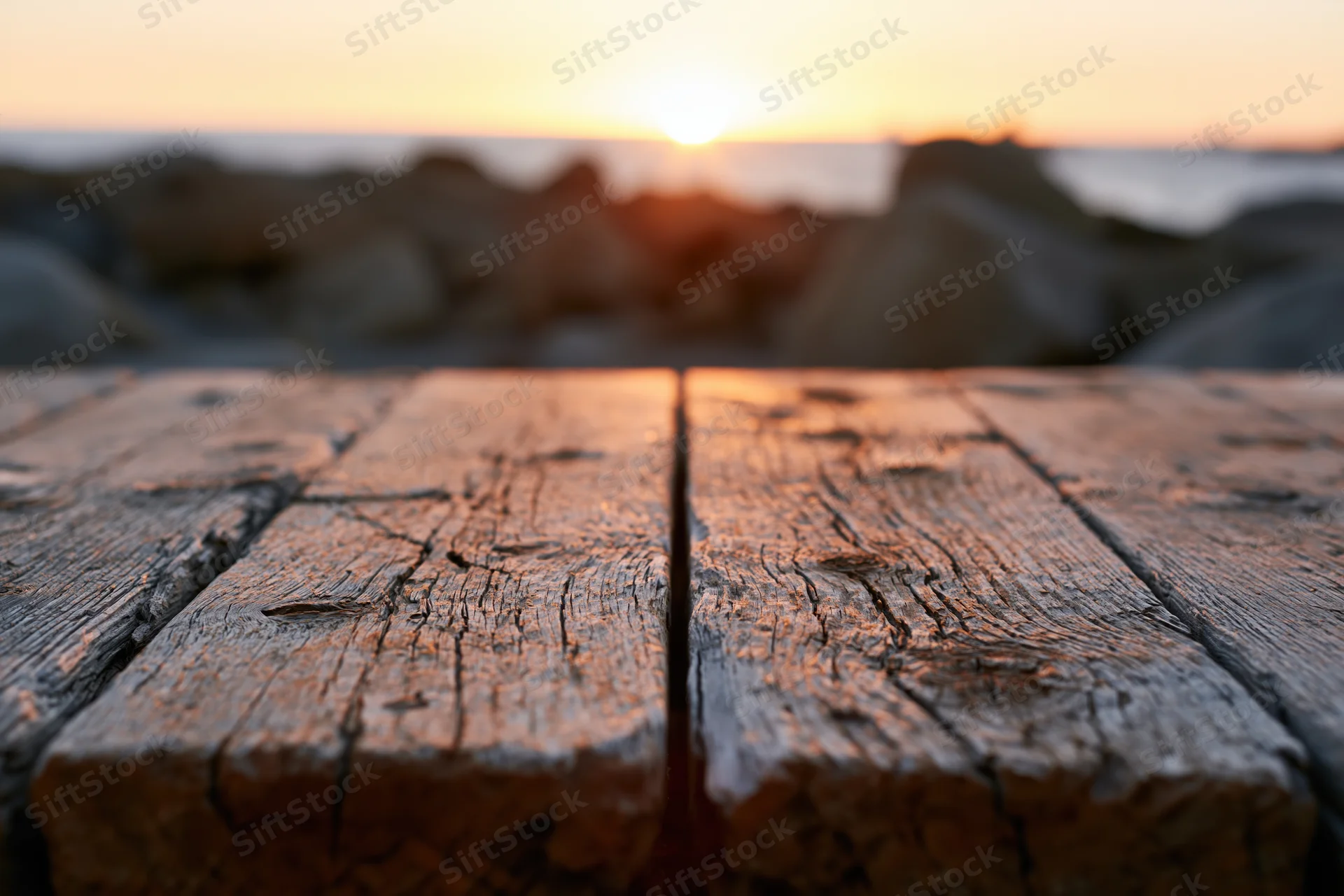Weathered wooden planks in foreground with sunset over ocean and rocks in background