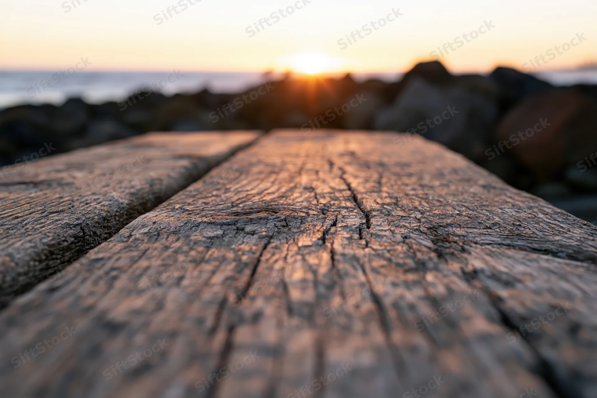 Weathered wooden plank surface leading toward sunset over ocean at dusk