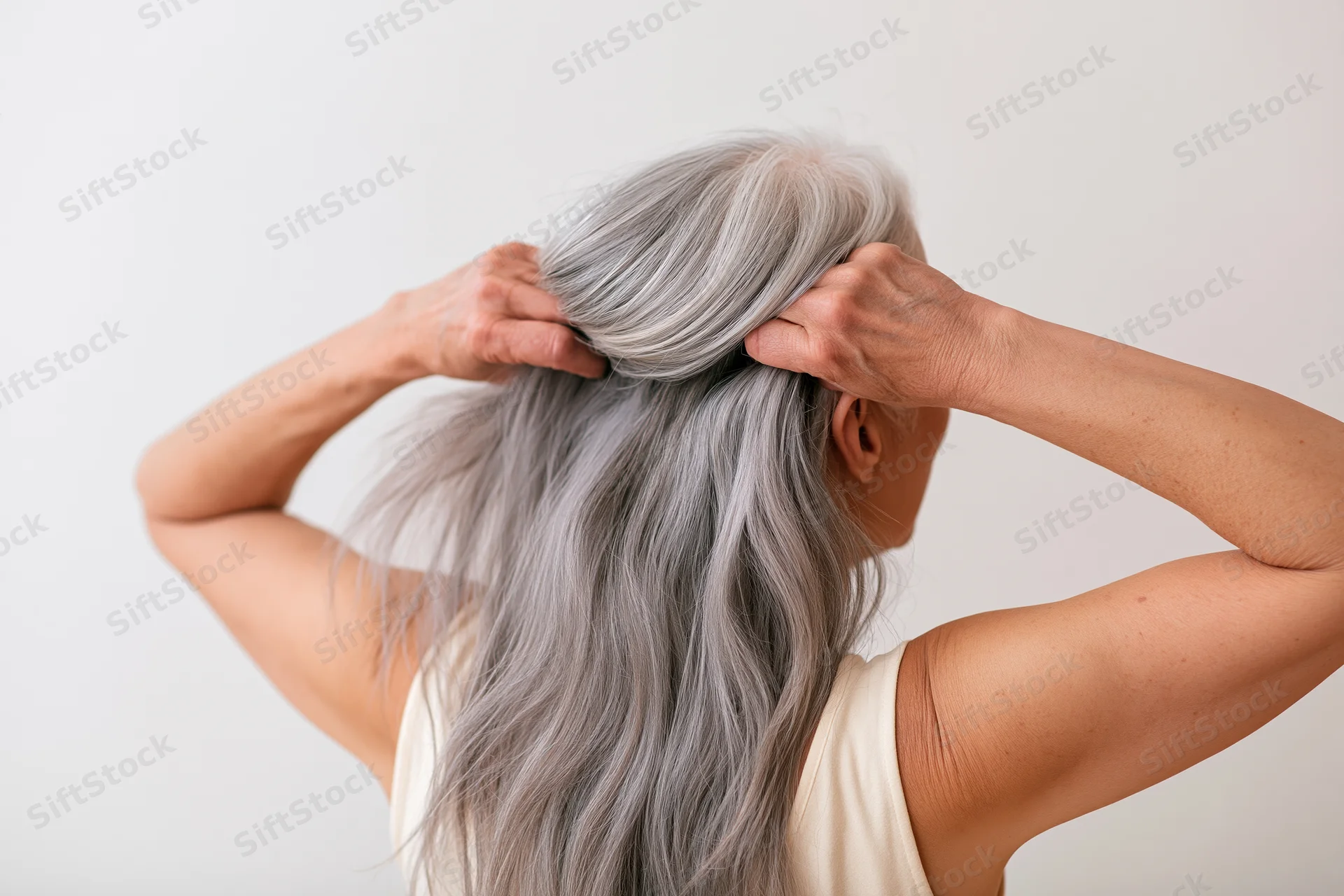 Senior woman holding her long silver-grey hair from behind in a studio setting