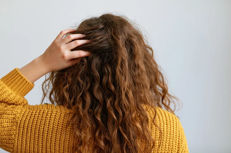 Woman from behind touching her long curly hair while wearing a yellow knit sweater