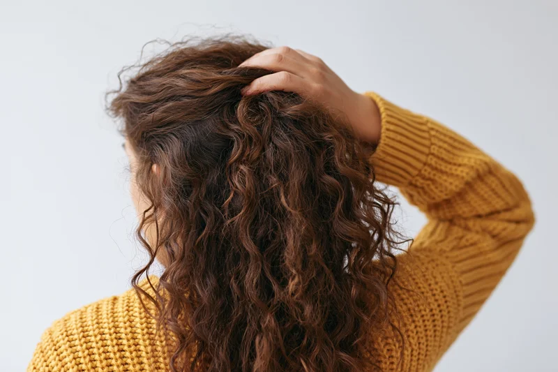 Woman from behind touching her long curly hair while wearing a yellow knit sweater