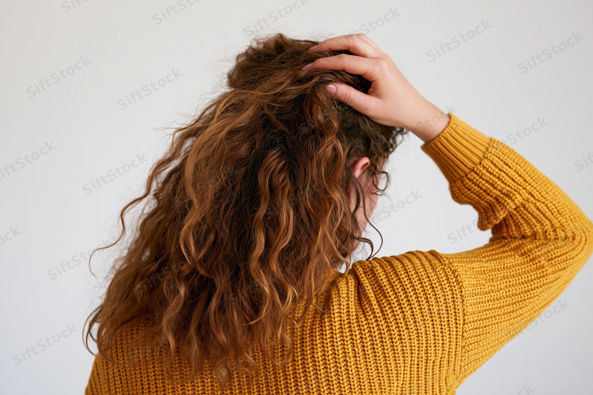 Woman from behind touching her long curly frizzy hair while wearing a yellow knit sweater