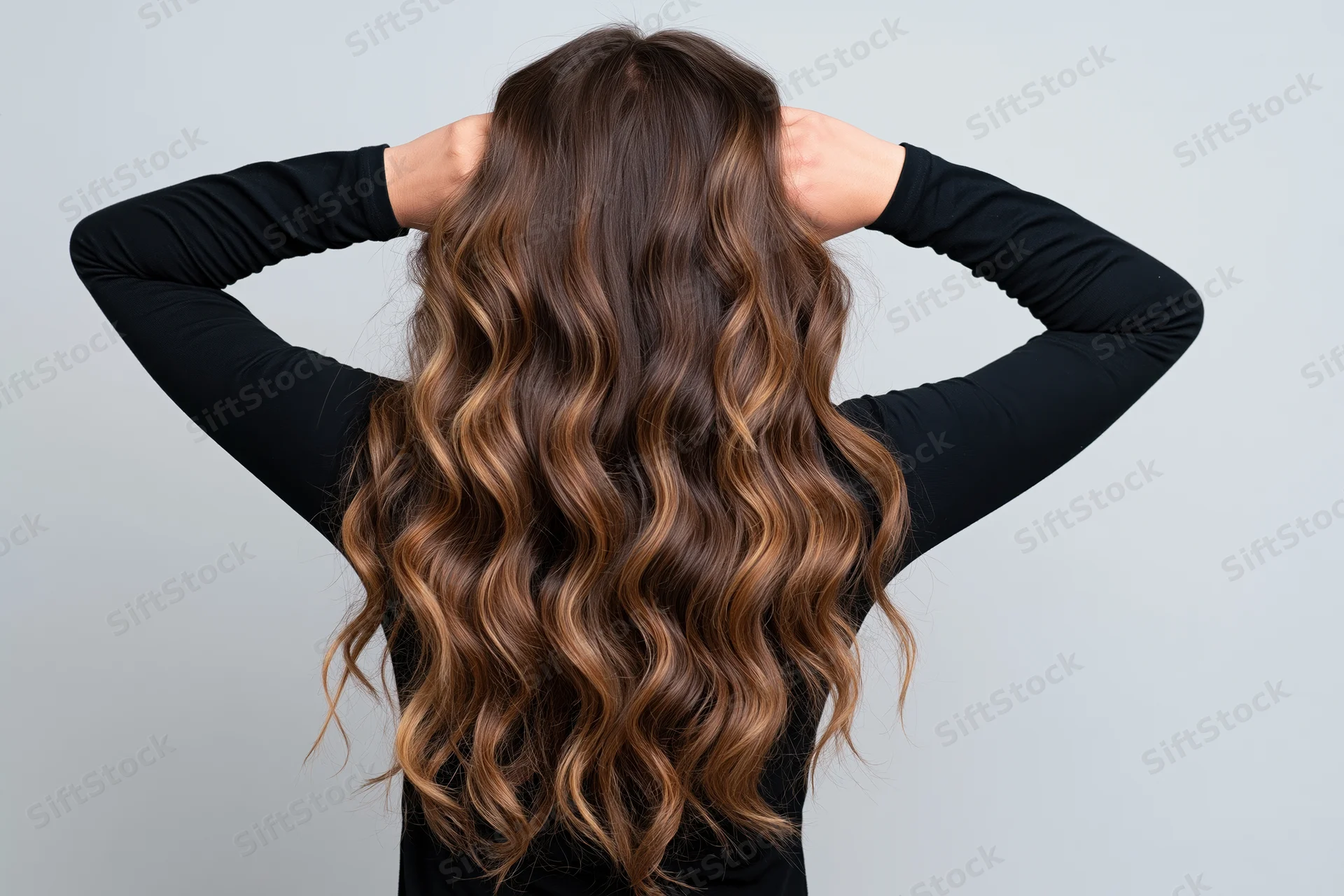 Woman from behind with hands raised to her head showing long wavy brown ombre hair