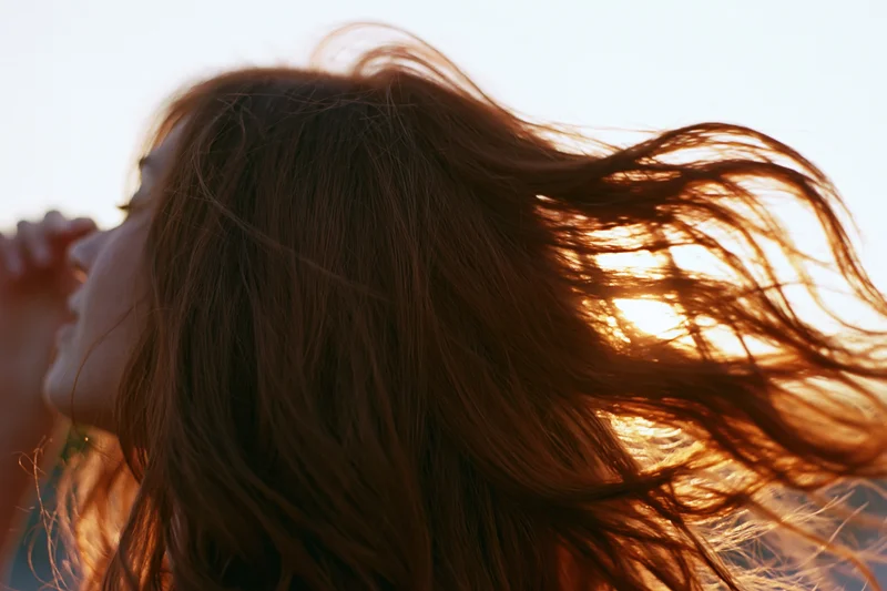 Woman tossing her long auburn hair in wind against sunset sky